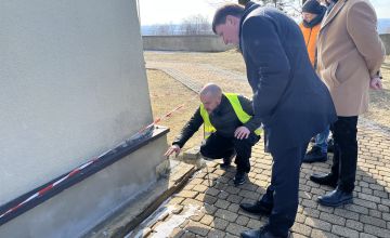 Zdjęcie przedstawiające mury kościoła oraz czterech mężczyzn. Jeden z nich kuca pokazując częściowo odsłonięte fundamenty kościoła, drugi mężczyzna stoi nachylony obserwując i słuchając wypowiedzi mężczyzny kucającego przy fundamentach.